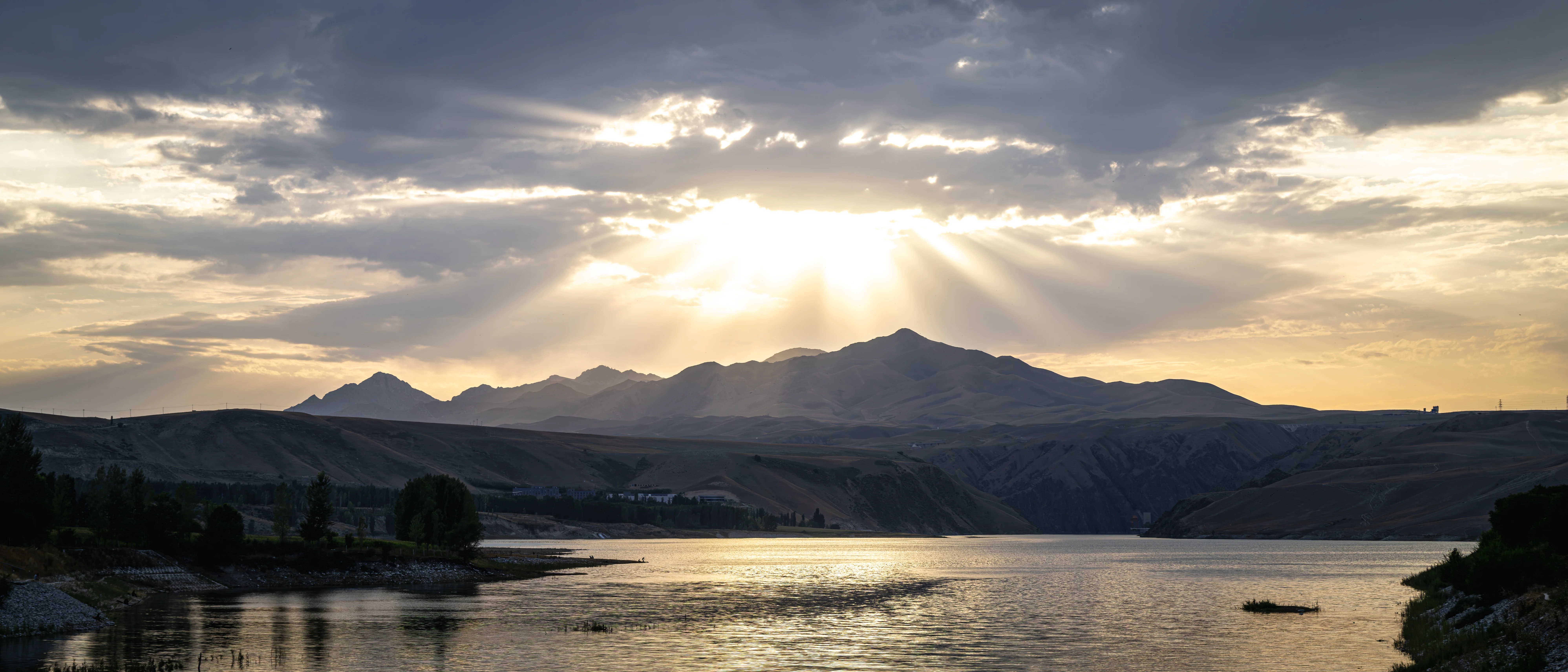 Sunset light falling in columns over the Tianshan range and a reservoir